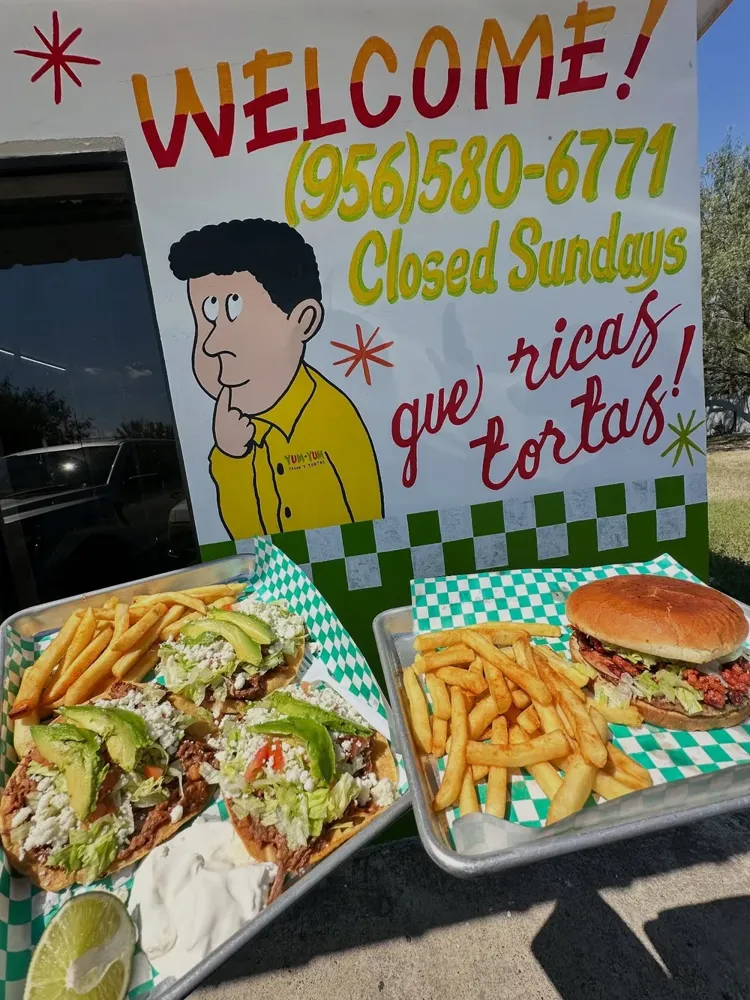 The YUM-YUM welcome sign with plates of tostadas, fries and a burger
